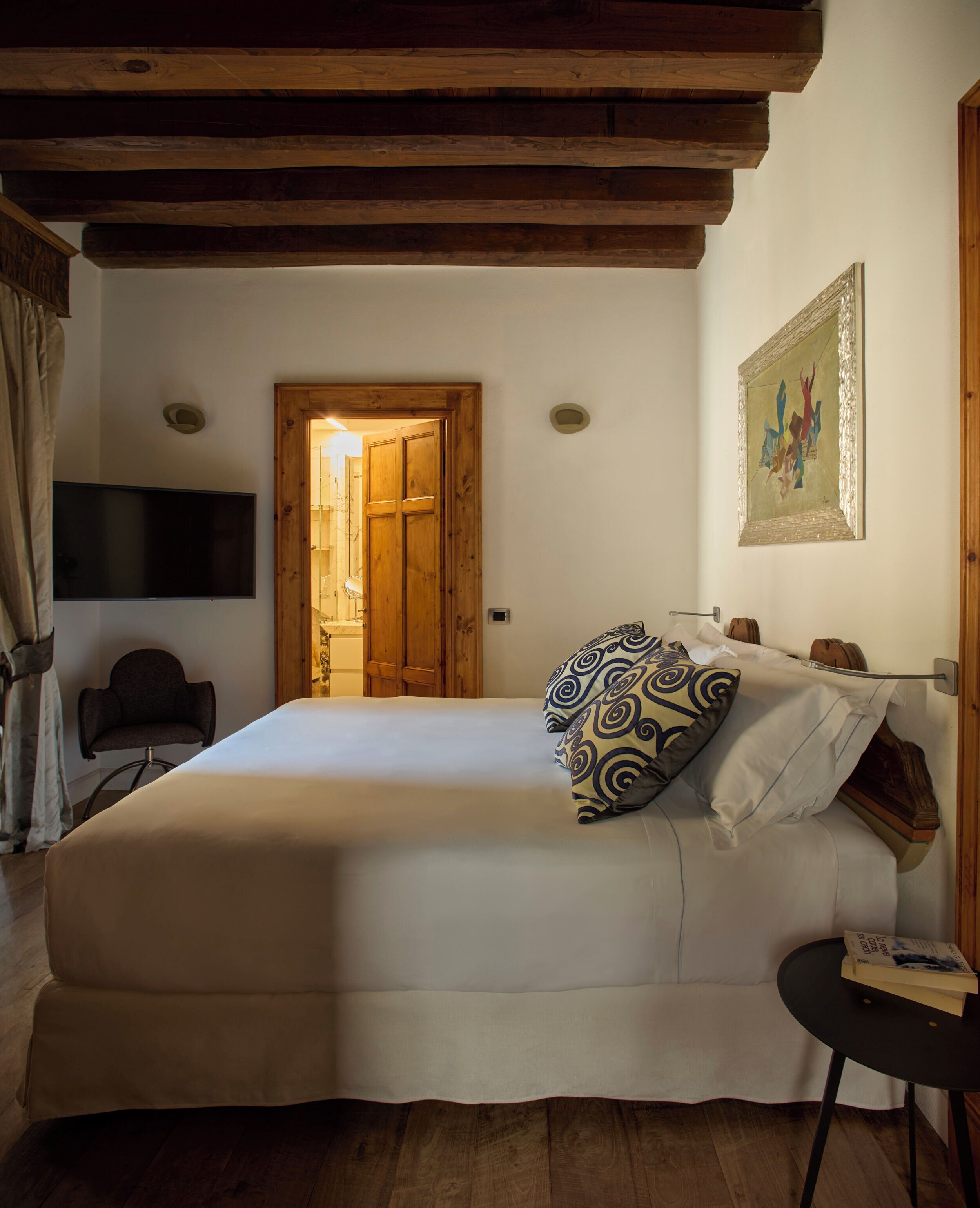 Un dormitorio con cama, una silla, un televisor y techo de madera.