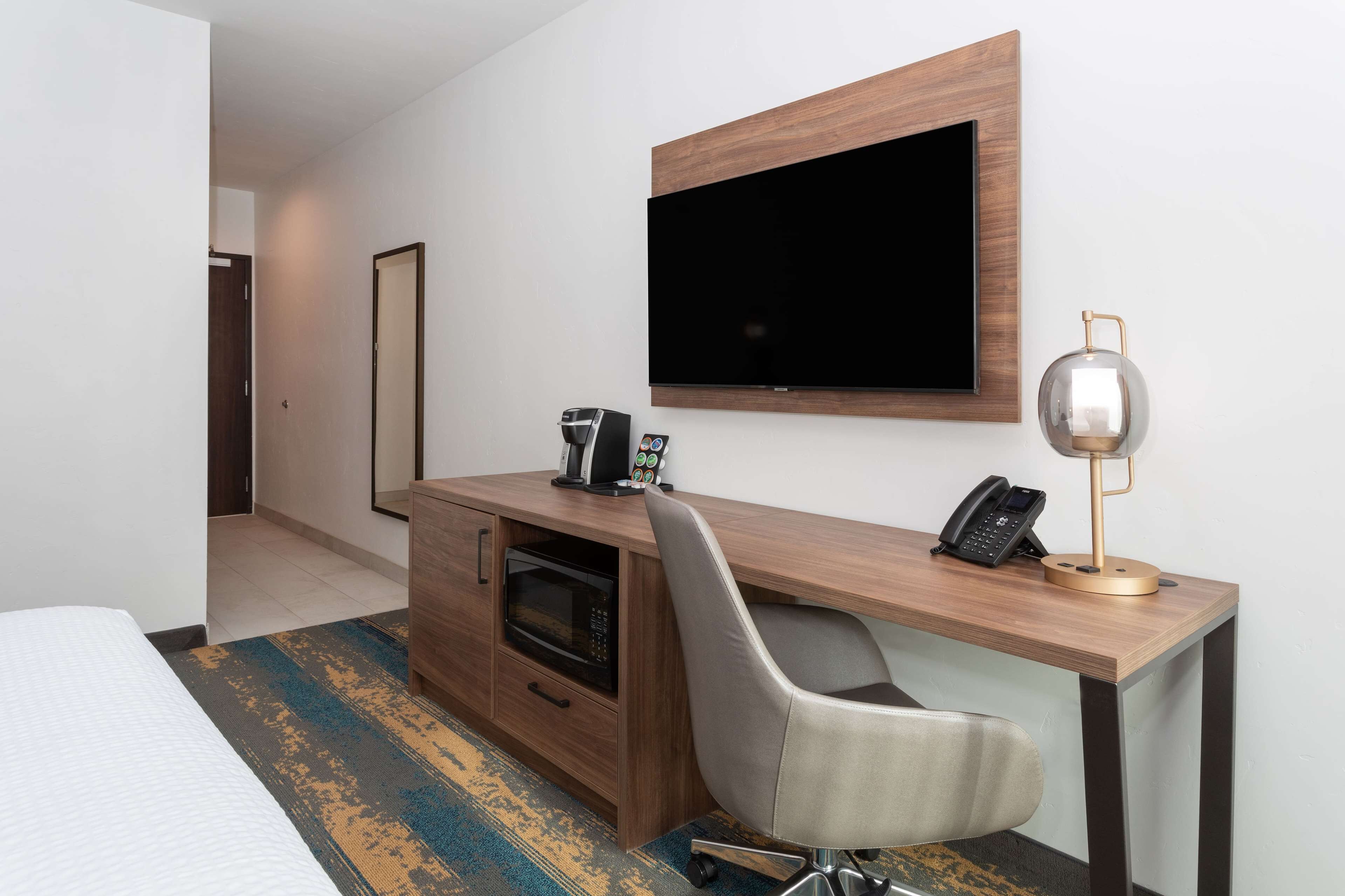 A hotel room with a wooden desk, a flat-screen TV, a coffee machine, a phone, and a microwave.