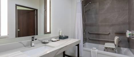 A modern bathroom with a large mirror, two sinks, a shower with grab bars, and a bathtub.