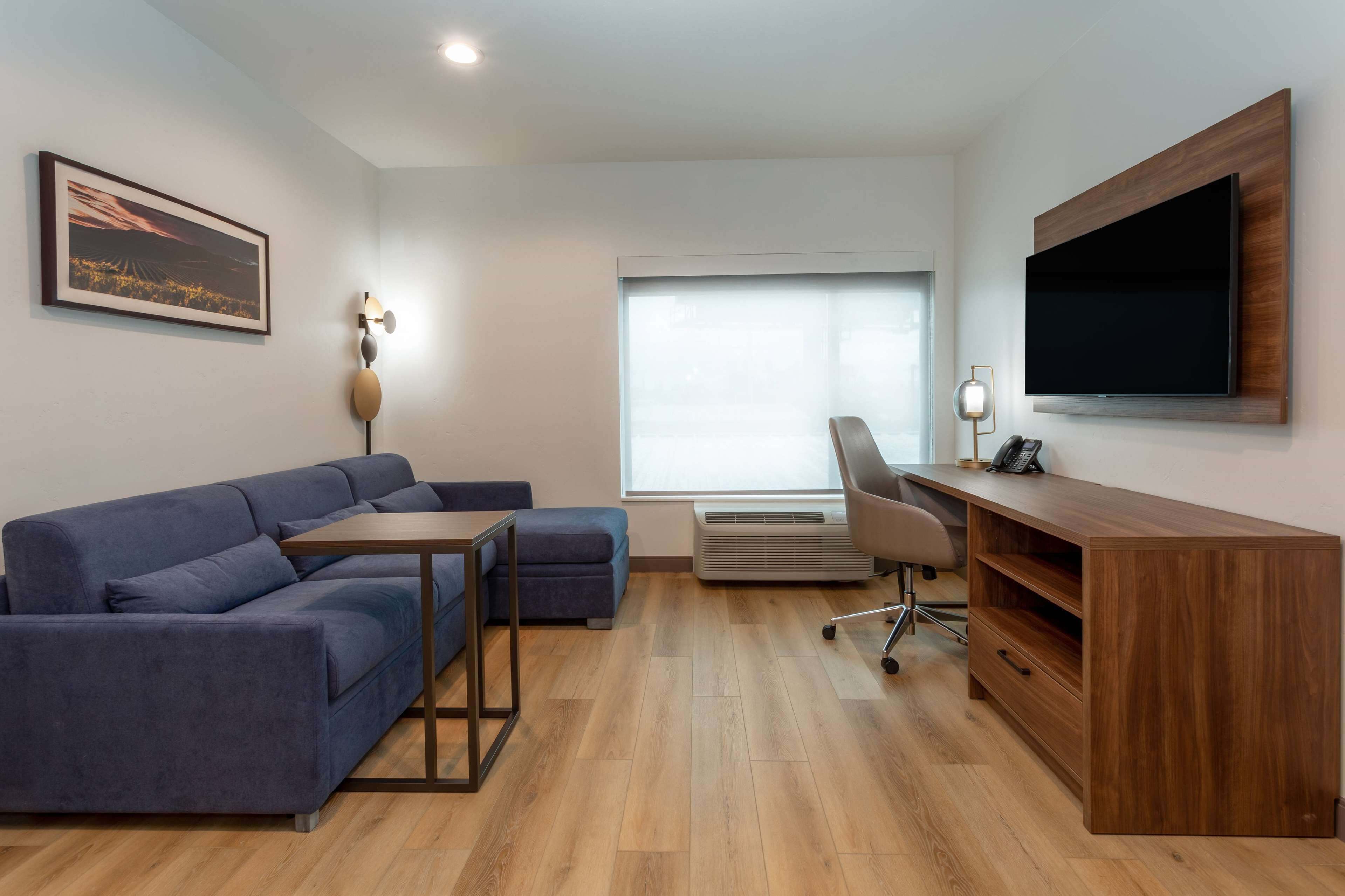 Una sala de estar moderna con un sofá azul, un escritorio de madera, un televisor de pantalla plana y un ventanal grande.