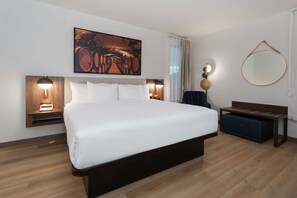 Ett modernt hotellrum med en stor säng, två sängbord med lampor, en spegel som hänger på väggen och en träbänk.
