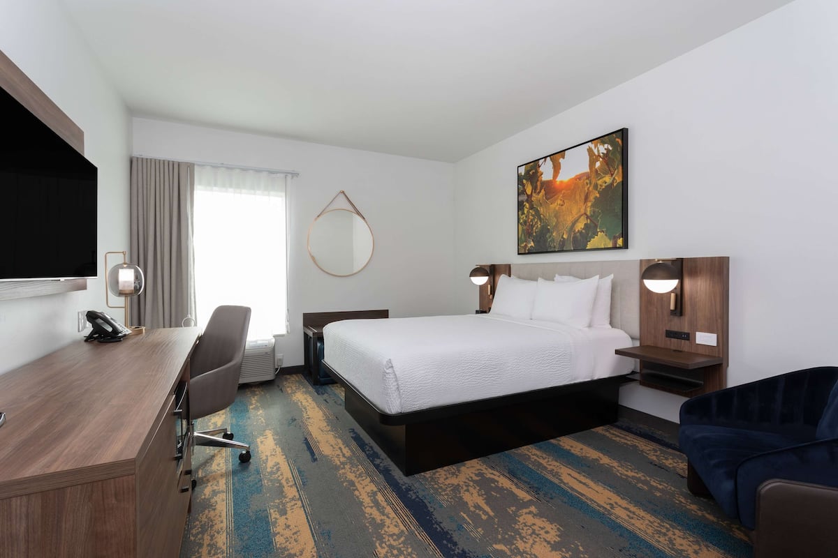 A hotel room with a bed, desk, chair, and a large painting on the wall.