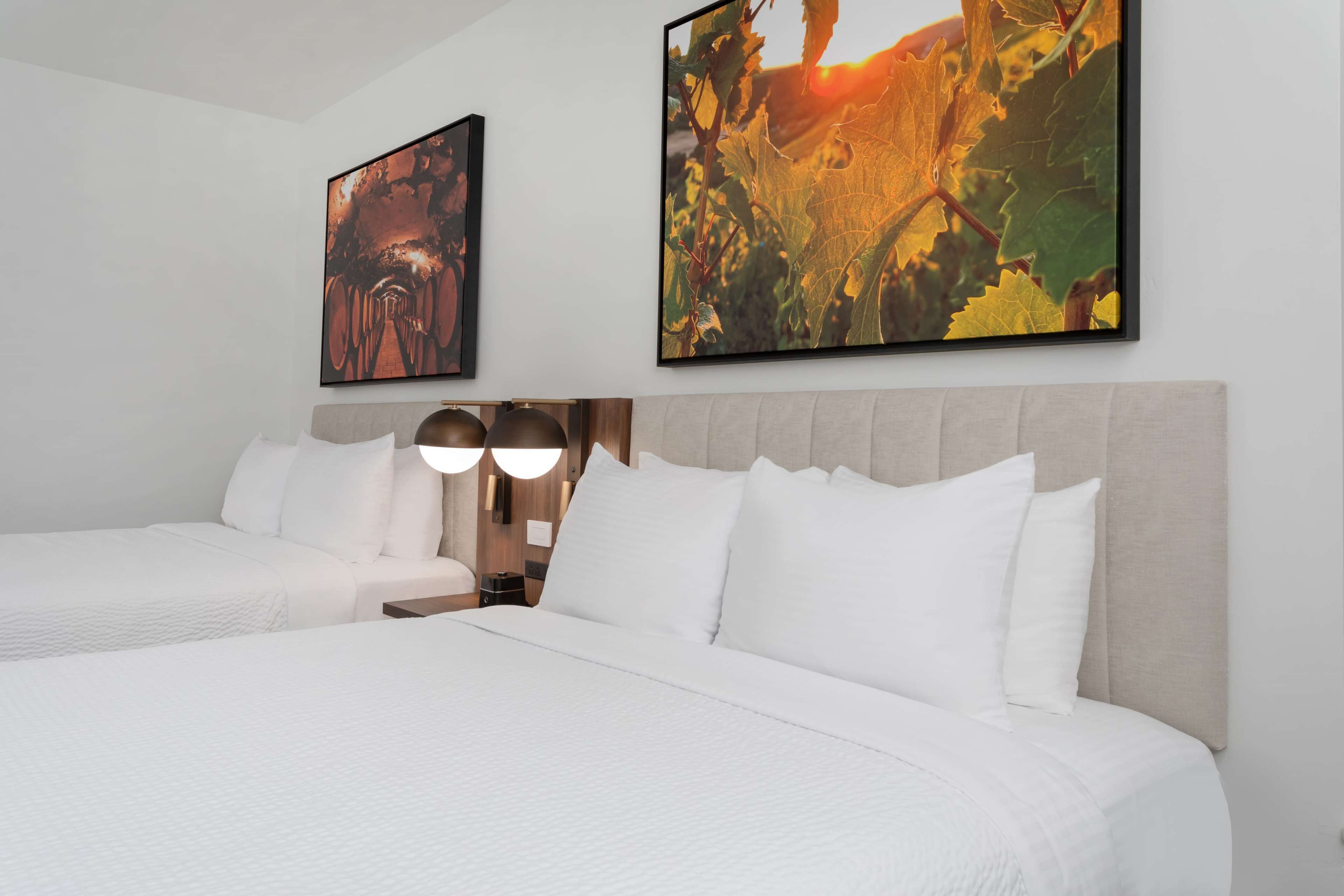 A hotel room with two beds, a large window, and two wall-mounted artworks.