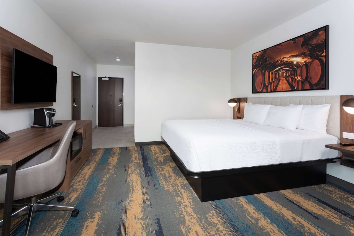 A hotel room with a bed, a desk with a computer, a TV, and a painting on the wall.