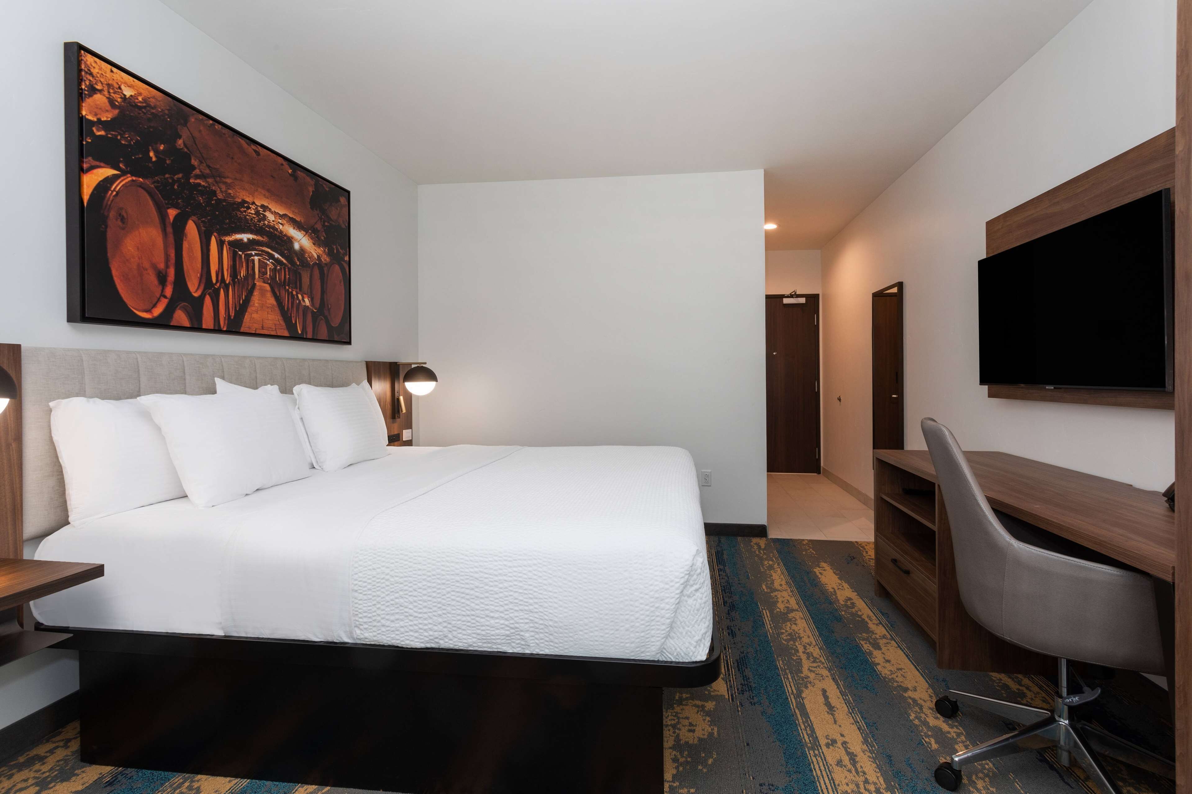 Habitación de hotel con una cama grande, un escritorio con silla, un televisor de pantalla plana y un cuadro en la pared.