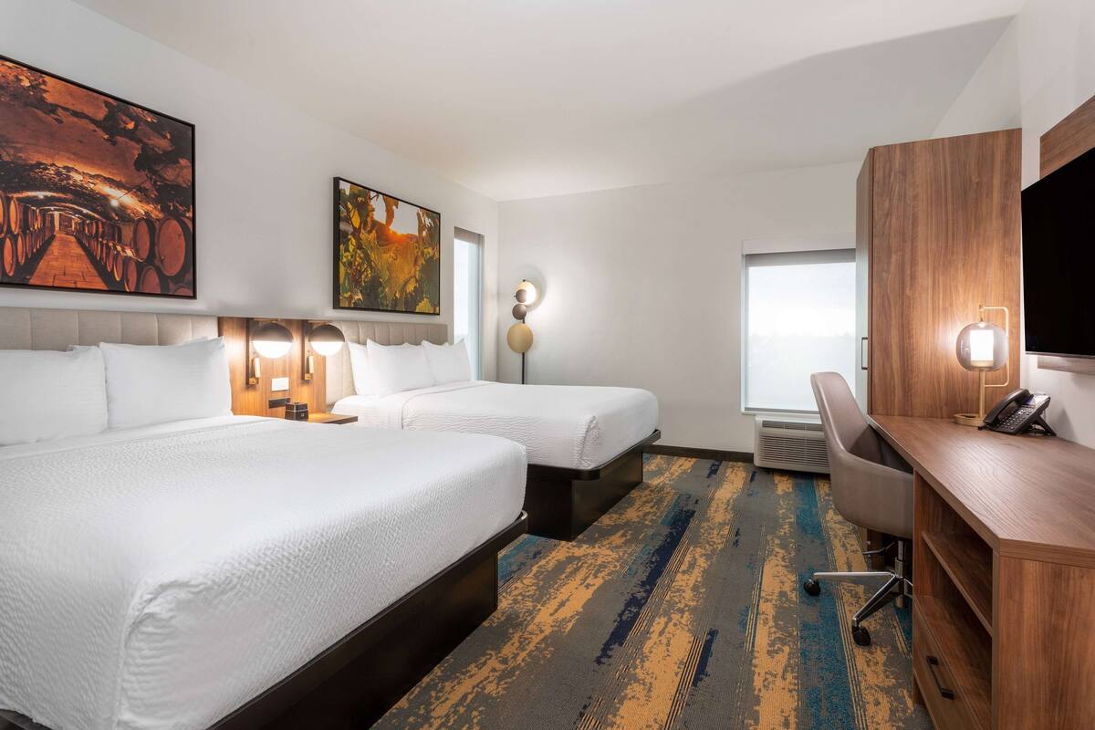 A hotel room with two beds, a desk, a chair, and a TV.