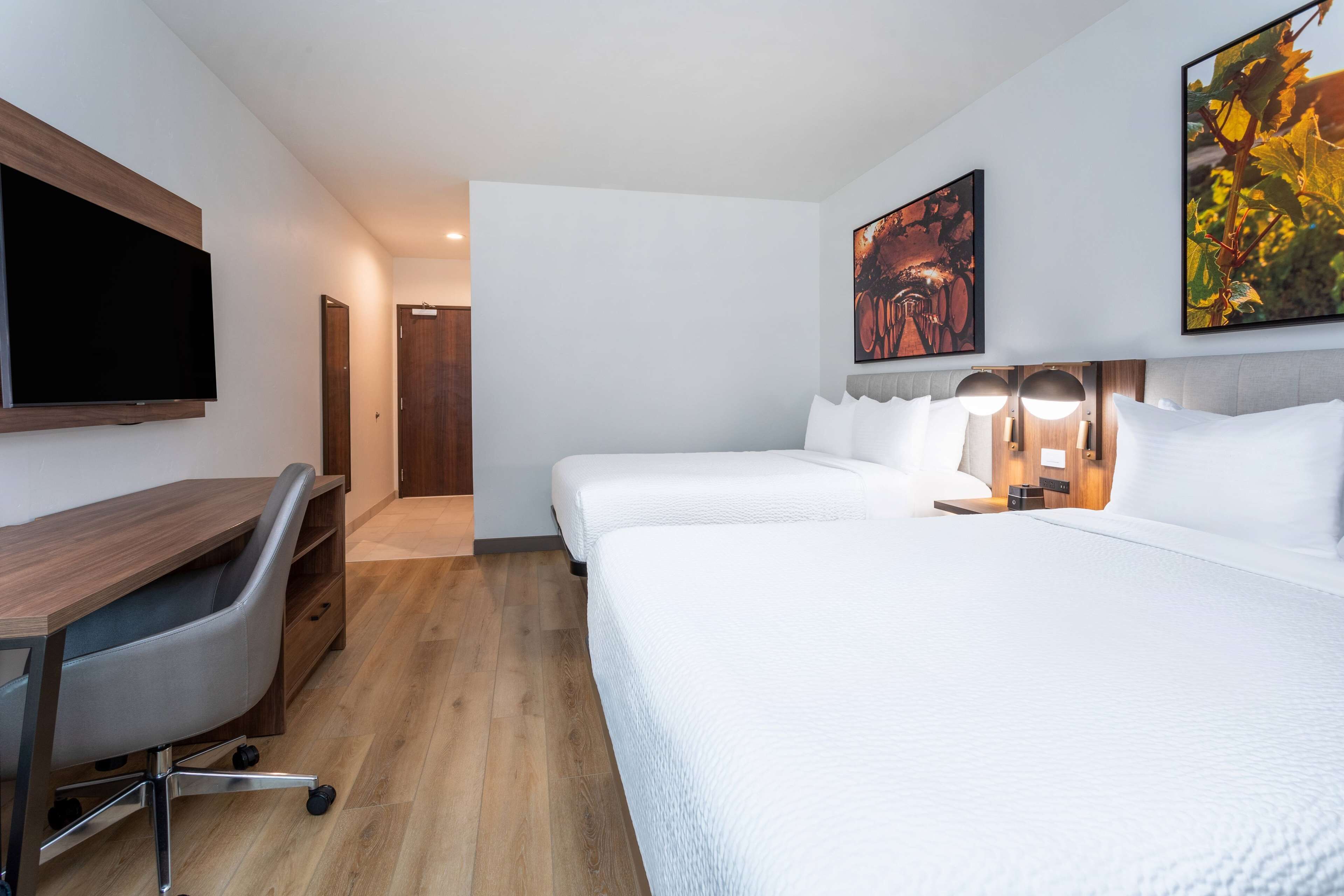 Une chambre d’hôtel équipée d’un bureau, de deux lits, d’une télévision et d’œuvres d’art accrochées aux murs.