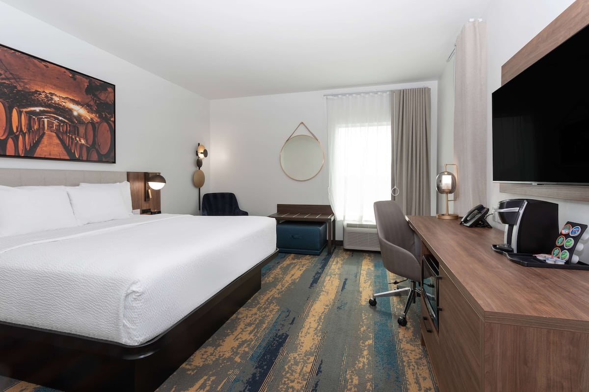 A hotel room with a large bed, a desk with a coffee maker, a TV, and a large painting on the wall.