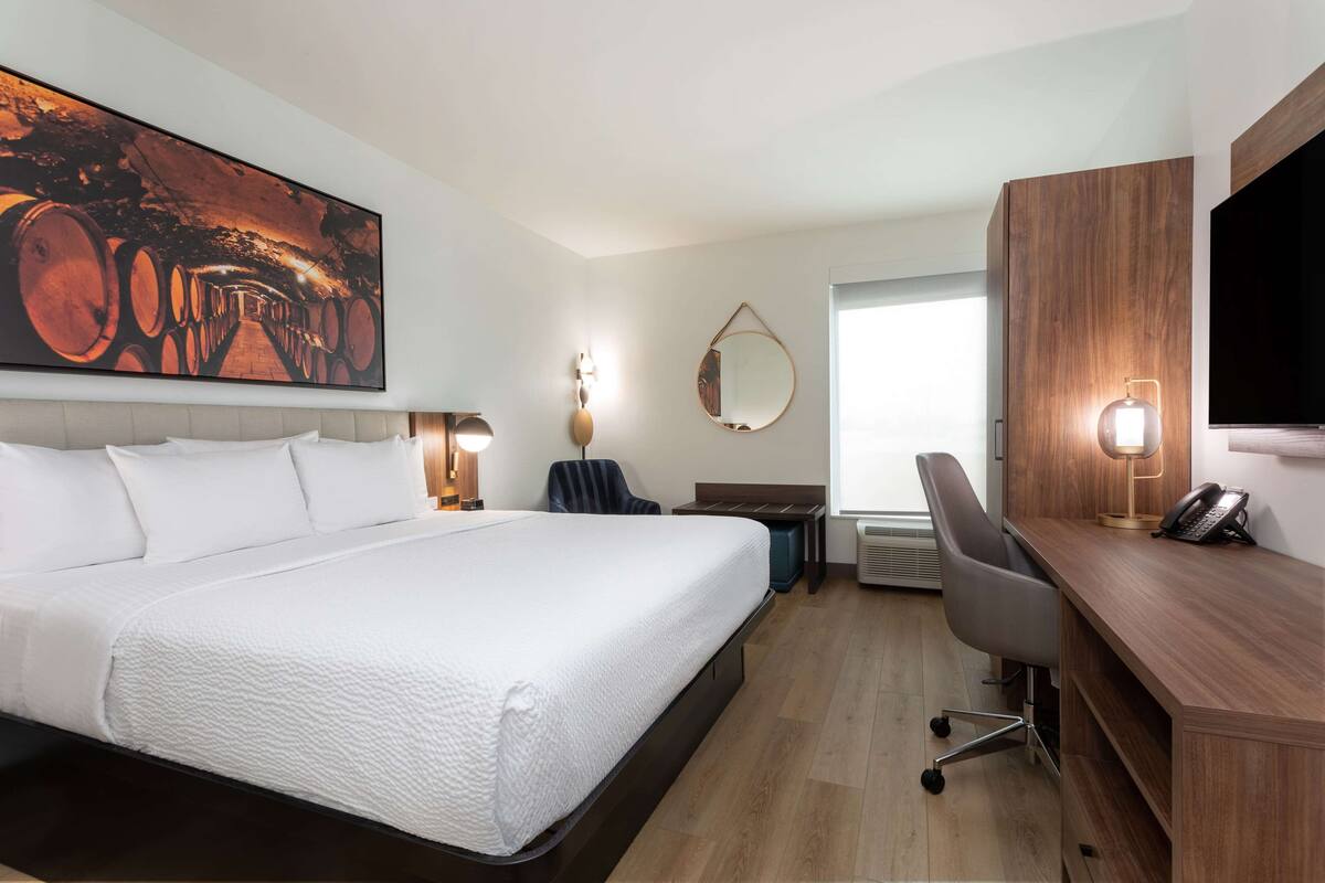 A hotel room with a large bed, a desk with a chair, a television, and a large painting on the wall.