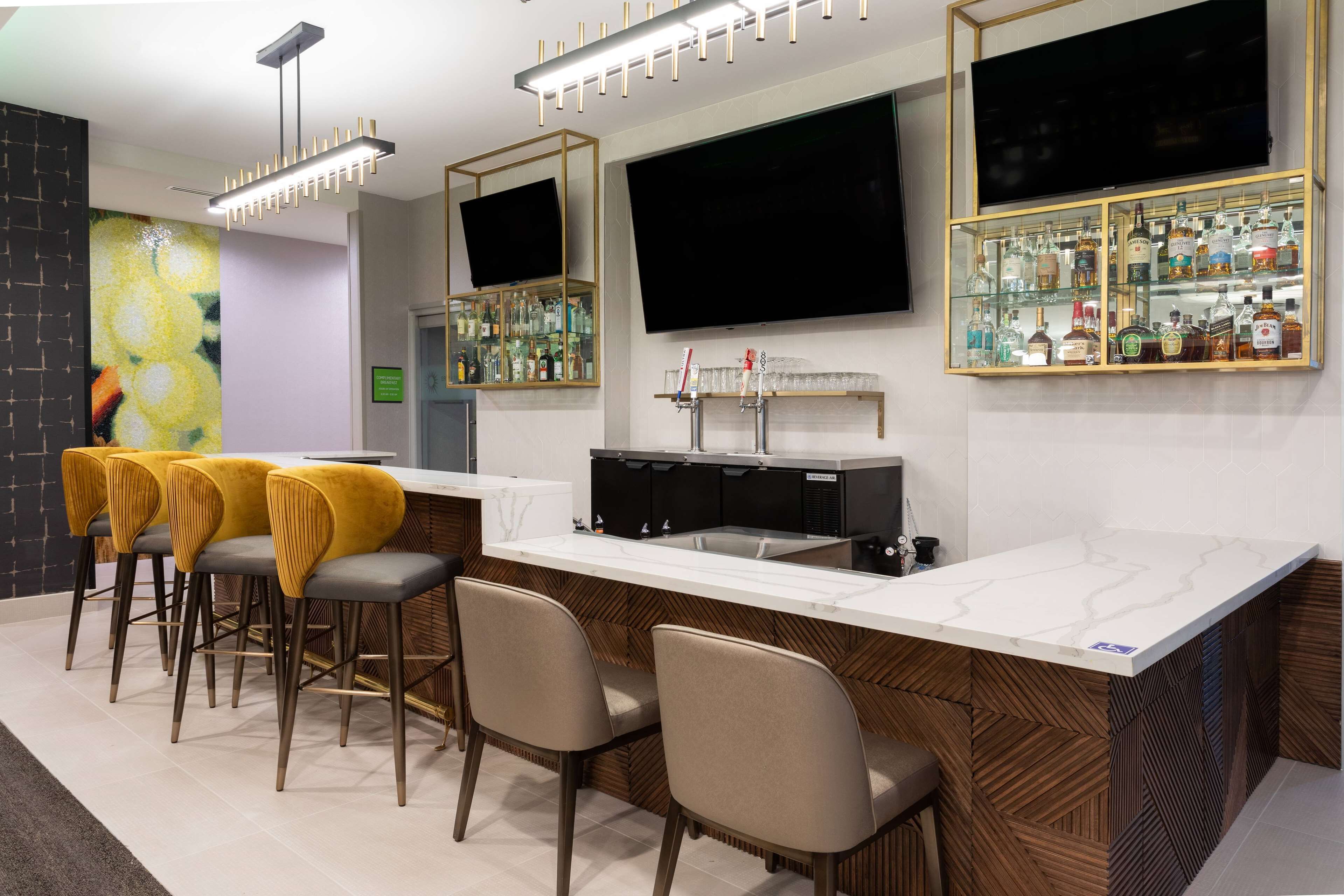 A bar area with a marble countertop, bar stools, a television, and a liquor display.