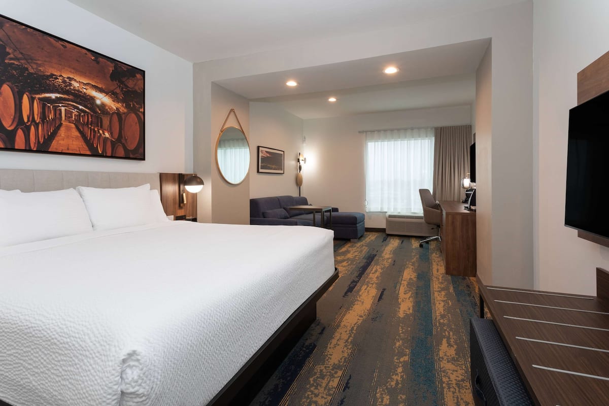 A hotel room with a large bed, a desk, a chair, a TV, and a painting on the wall.