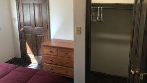 A room with a wooden door, a wooden dresser, and a bed with a red cover. - Serene location in middle of wine country  (Westfield)