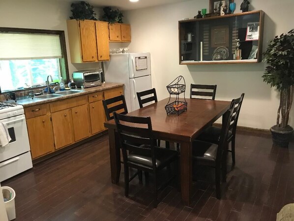 Una cocina con armarios de madera, microondas, refrigerador y una mesa de comedor con sillas.