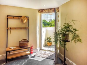 A hallway with a wooden shelf holding a hat and a basket, a fire extinguisher, and a potted plant. - 1 bedroom accommodation in Tavistock (Tavistock)