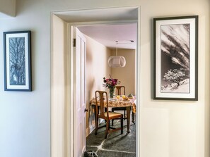 A dining area with a table set for two, a vase with flowers, and framed artwork on the walls. - 1 bedroom accommodation in Tavistock (Tavistock)
