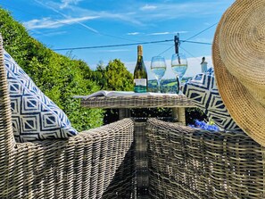 Wicker furniture with geometric patterned cushions, a table with a bottle and glasses, and a large straw hat. - 1 bedroom accommodation in Tavistock (Tavistock)