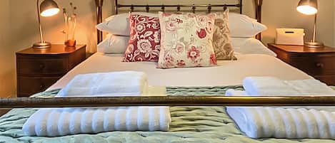 A neatly made bed with floral pillows, a bedside table with a lamp, and a nightstand with a lamp.