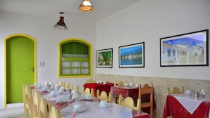 A dining area with tables set for a meal, a green door, and framed pictures on the wall. - Pousada Pôr do Sol (Paraty)