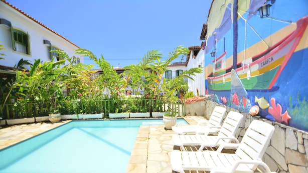 A pool area with lounge chairs, a mural of a boat, and a stone wall. - Pousada Pôr do Sol (Paraty)