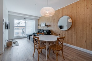 Een moderne woonkamer met een ronde eettafel, rieten stoelen, een grote spiegel en een houten wand.