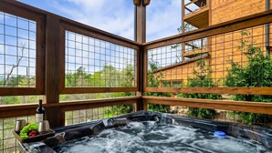 Un bain à remous doté d’une terrasse en bois et de panneaux de verre, entouré de verdure.