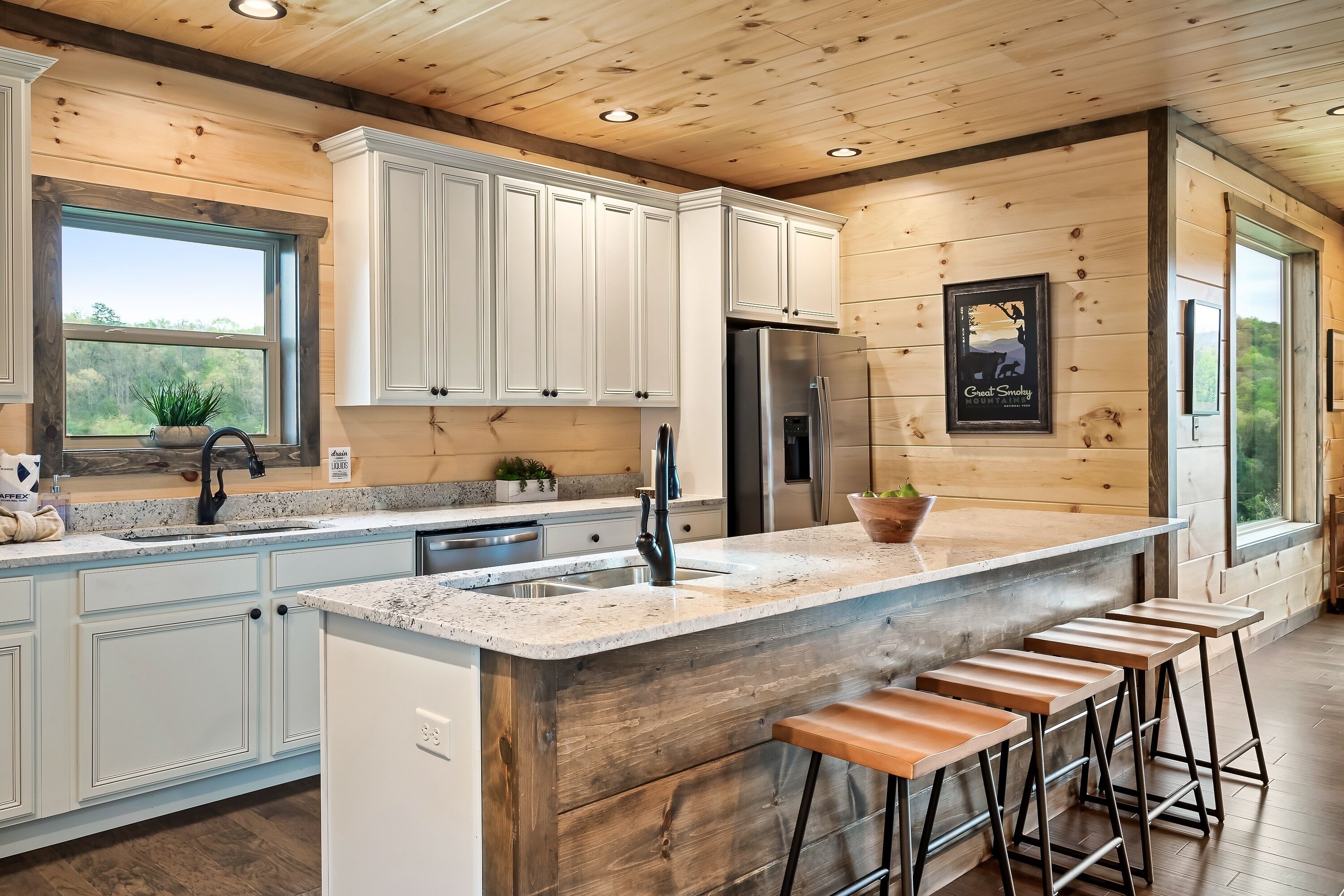 A modern kitchen with wooden cabinetry, a stainless steel refrigerator, and a bar area with stools.