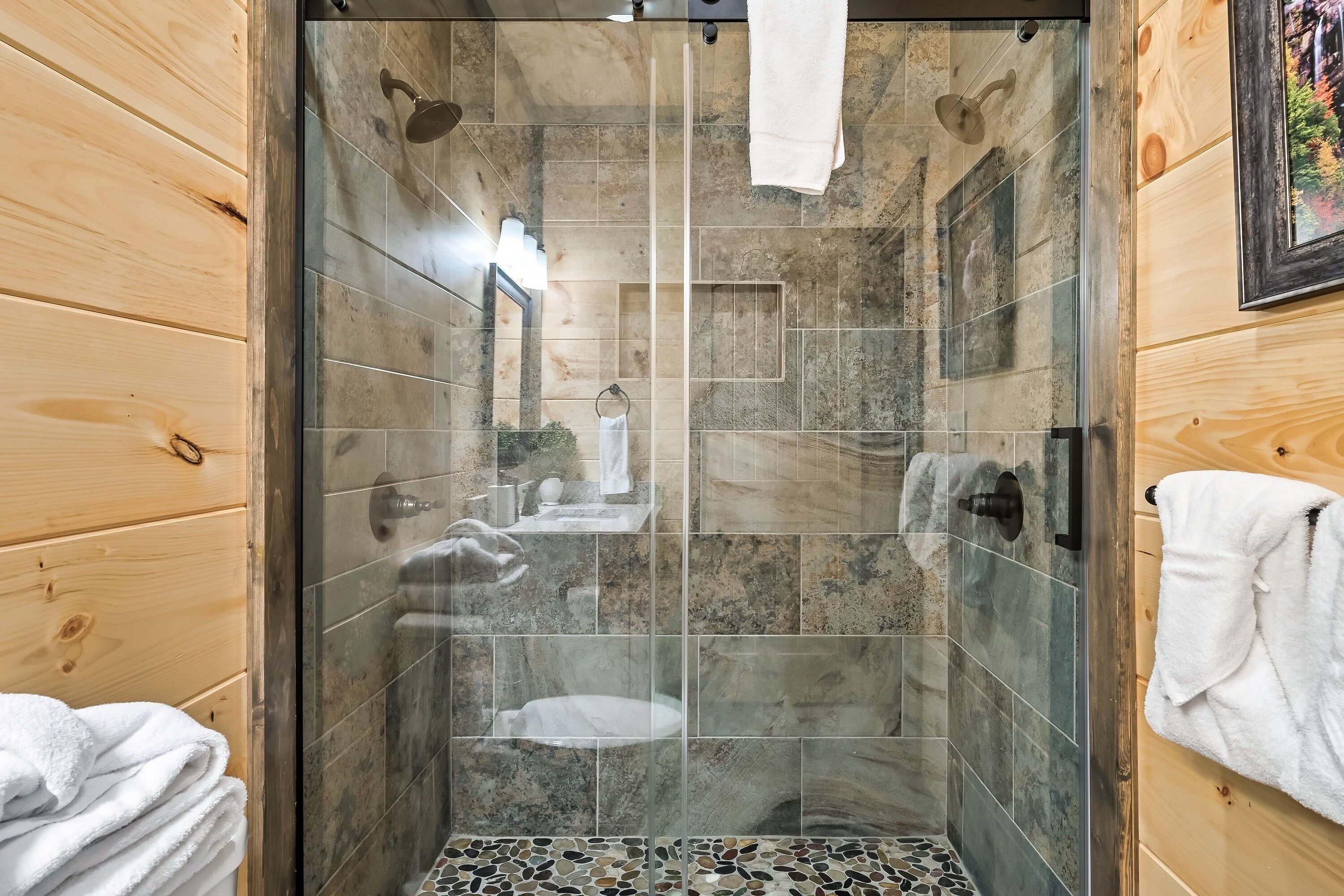 Une douche avec une porte en verre, des murs en bois et un sol carrelé.