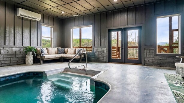 Un espace piscine agrémenté d’un mur en pierre, d’un coin salon avec des coussins et d’une vue sur l’extérieur.