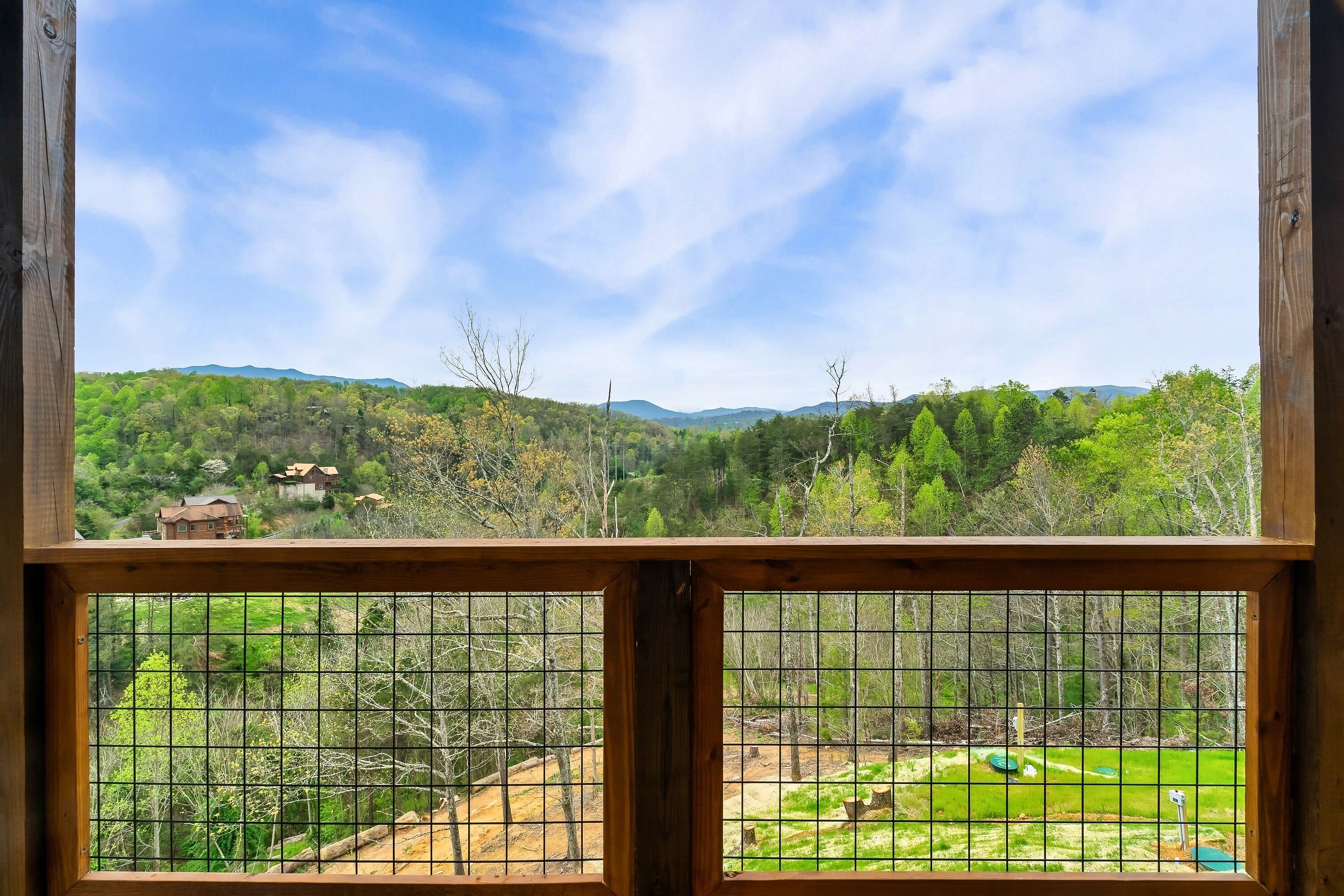 A view through a wooden-framed window with a grid pattern, overlooking a green landscape with trees and a distant house.