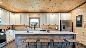 Une cuisine moderne avec un plafond en bois, des armoires blanches, un îlot central doté de tabourets et un réfrigérateur en acier inoxydable.