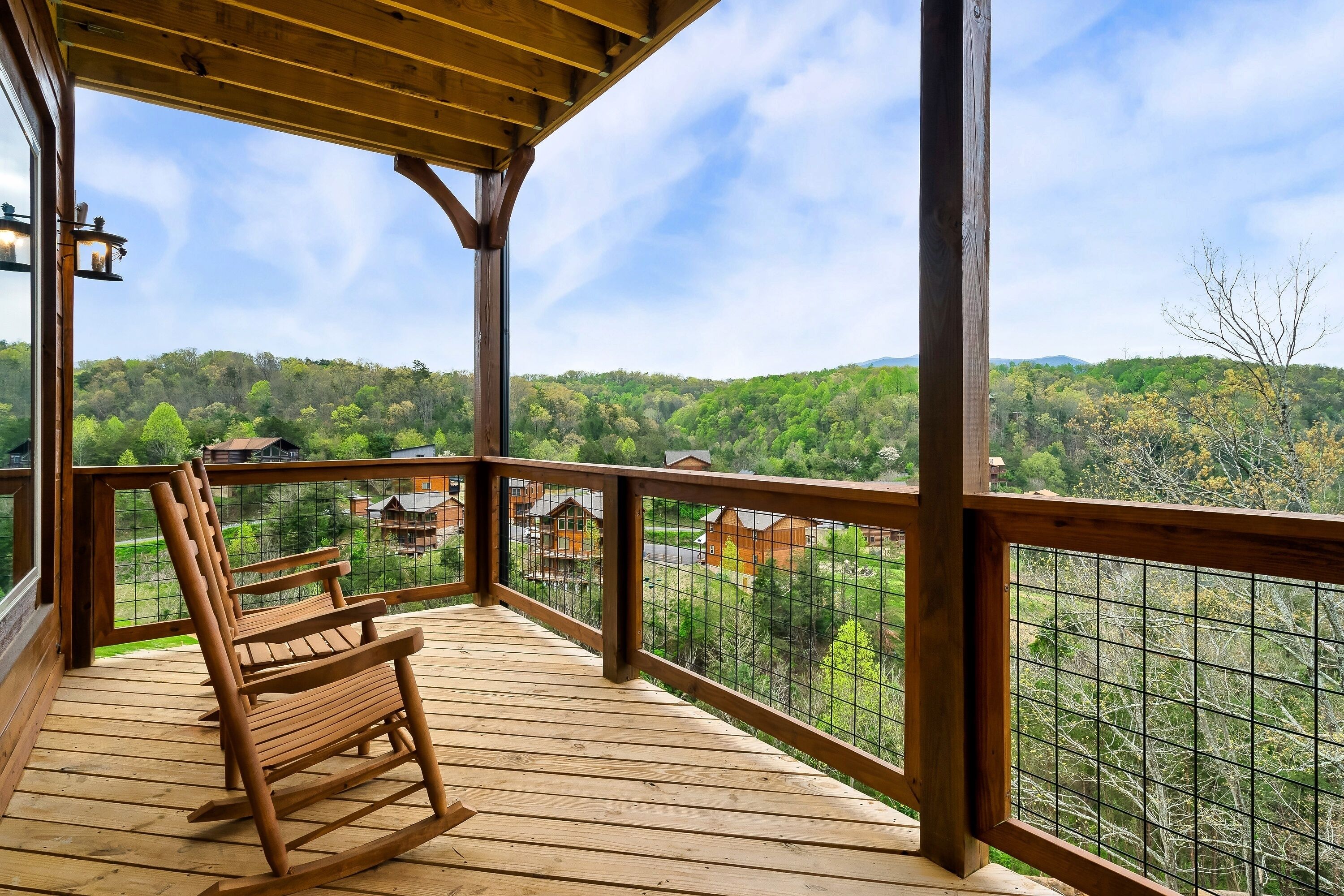 A wooden deck with a rocking chair, a wooden railing, and a view of a forested landscape.
