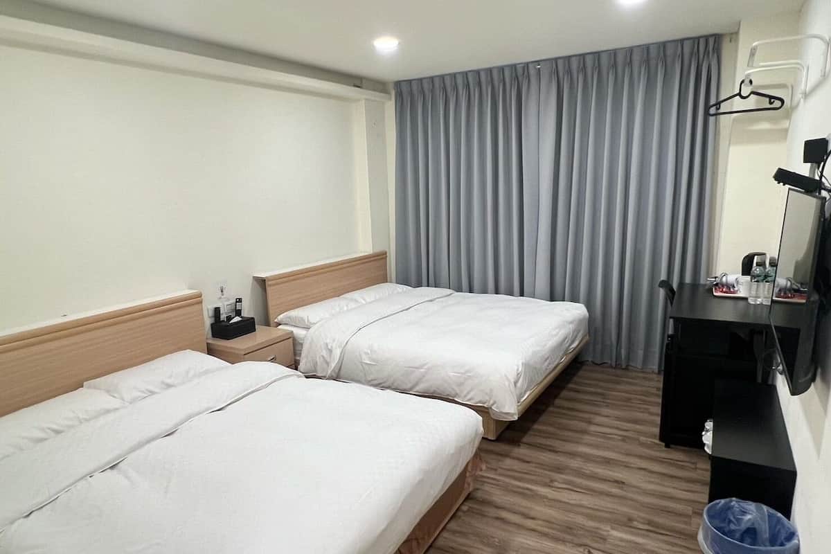 A hotel room with two beds, a desk, a chair, a mirror, a hanging light, and a blue trash bin.