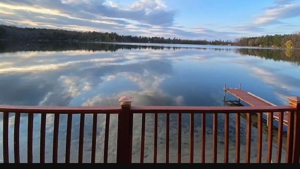 A calm lake with a wooden dock extending into the water, surrounded by trees and a clear sky. - Right On The Water (Wautoma)