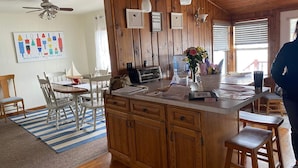 A wooden cabin interior with a kitchen island, white chairs, a striped rug, and a ceiling fan. - Right On The Water (Wautoma)