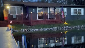 A house with a dock extending into a body of water, a front porch with railings, and an American flag. - Right On The Water (Wautoma)