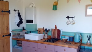A kitchen with a white refrigerator, a sink, a stove, and cabinets. There are kitchen utensils and a fire extinguisher on the counter. - stayinhartland @ Quincecote shepherds hut (Hartland)