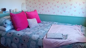 A bedroom with a teal headboard, patterned bedding, and a wall with bird wallpaper. - stayinhartland @ Quincecote shepherds hut (Hartland)