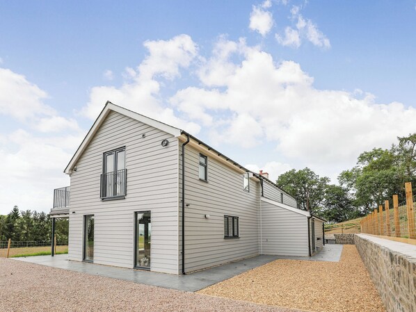 Une maison moderne à deux étages, dotée d’un toit en pente, de grandes fenêtres et d’une allée gravillonnée.