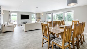 Een ruime woonkamer met een eettafel, houten stoelen, een bank en een televisie.