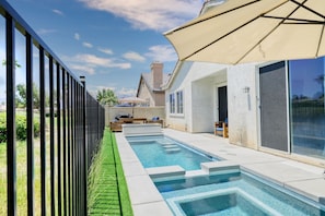 A swimming pool with a glass enclosure, a pergola with a beige canopy, and a view of a residential area.