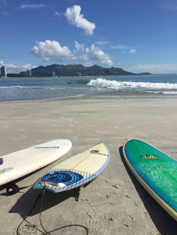 Three surfboards on a sandy beach with a view of the ocean and mountains in the background.