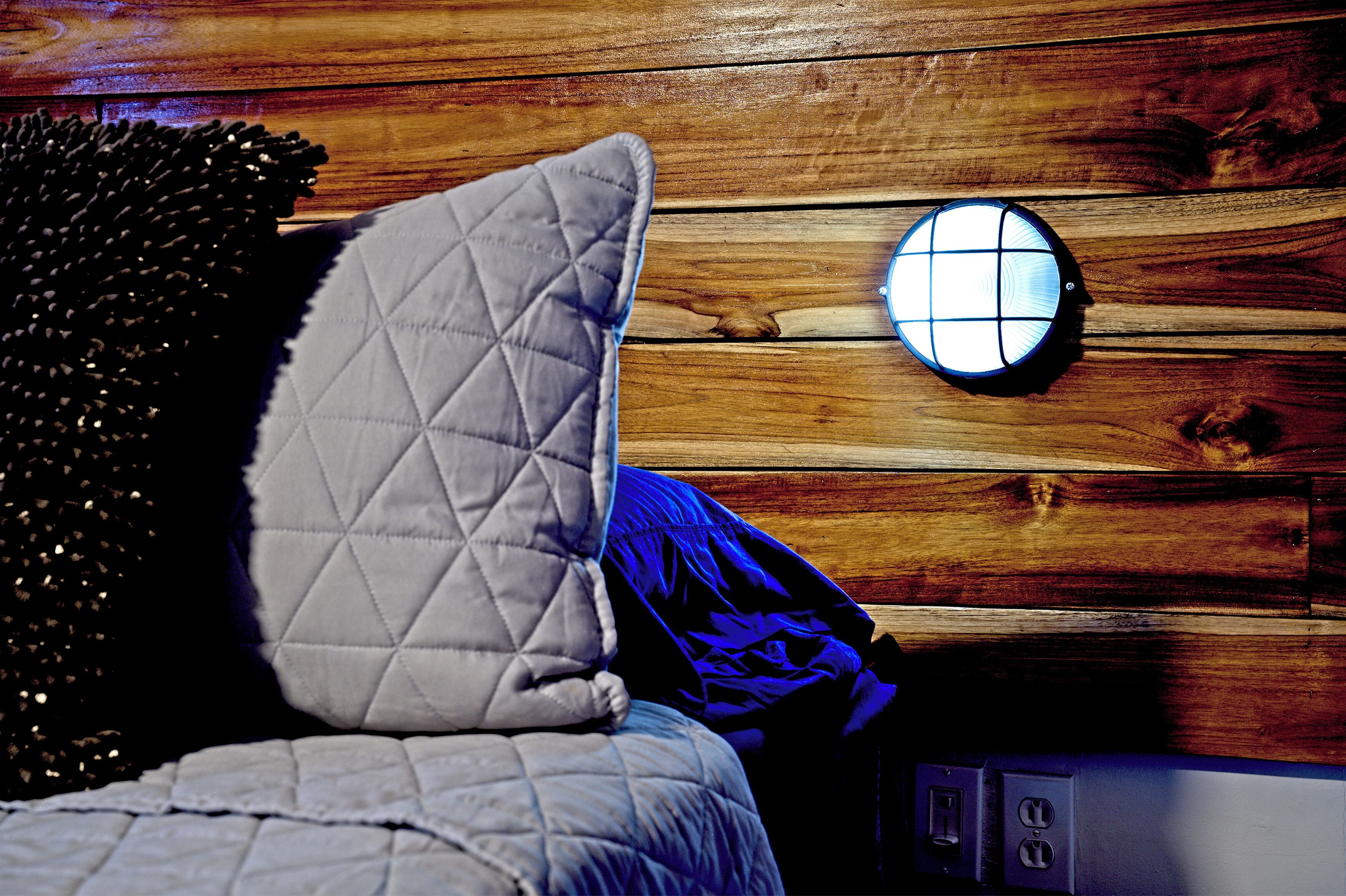 Un lit avec un oreiller matelassé et un luminaire rond fixé au mur.
