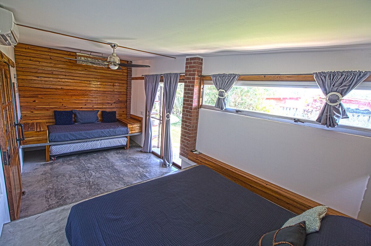 A room with a wooden wall, a bed, a window with curtains, and a ceiling fan.