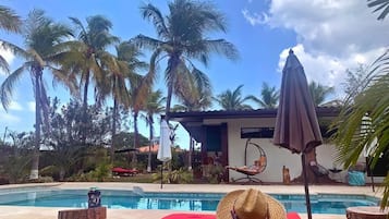 Un área junto a la piscina con una silla de relax roja, un sombrero de paja y una hamaca colgante.