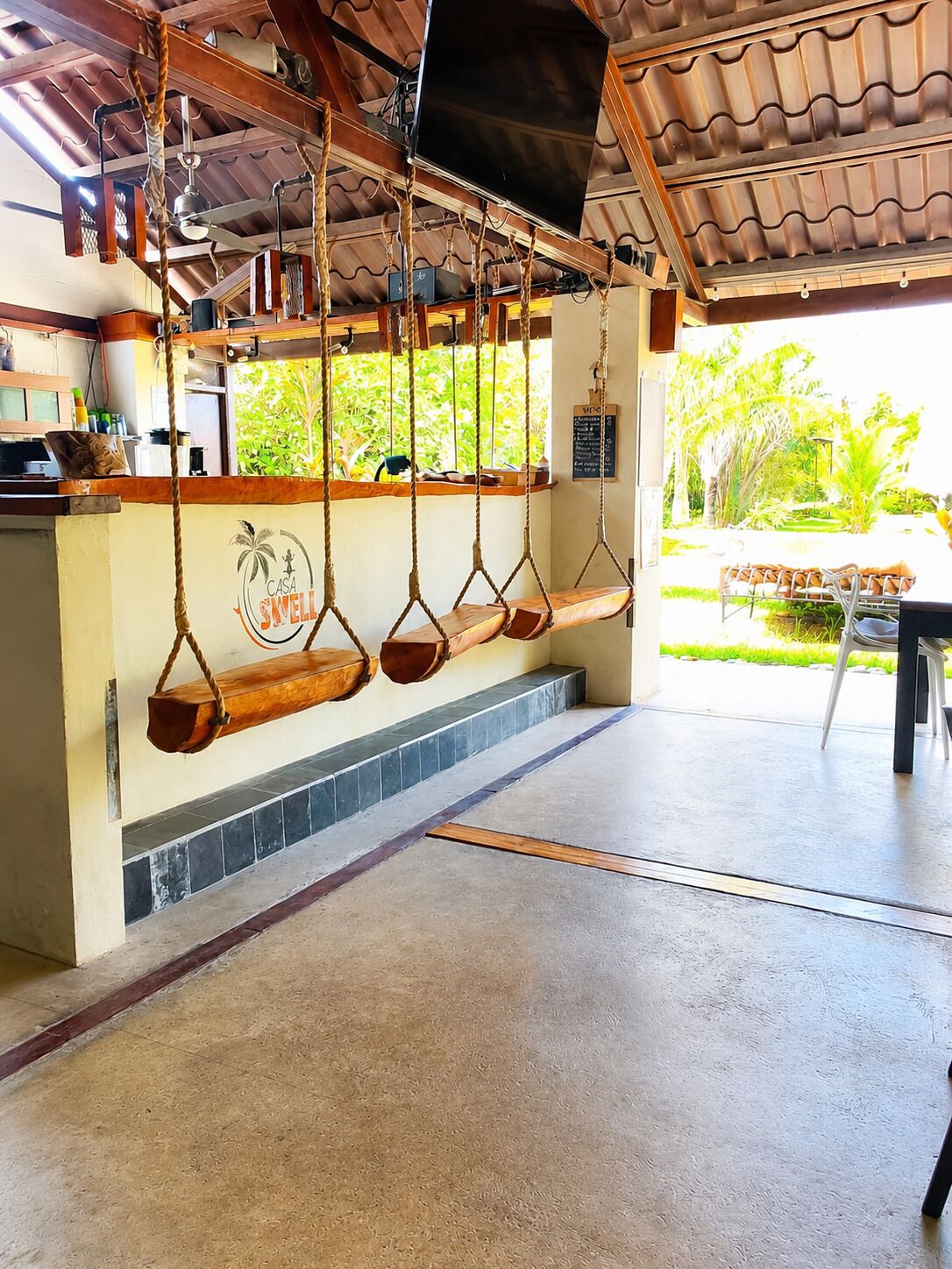 A room with a swing set, a wall-mounted TV, and a view of greenery outside.