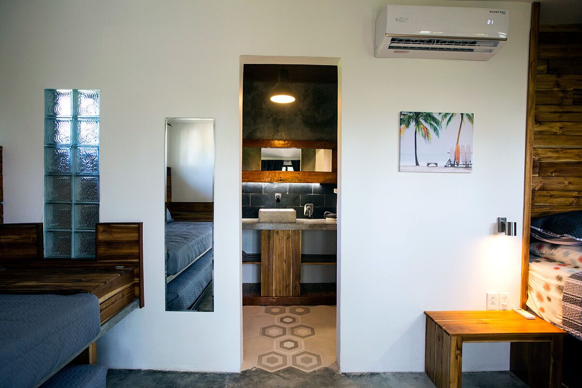 A compact room with a bunk bed, a small wooden table, a mirror, a sink, and a wall-mounted air conditioner.