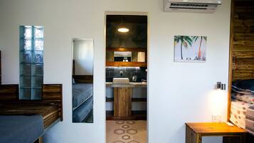 A compact room with a bunk bed, a small wooden table, a mirror, a sink, and a wall-mounted air conditioner.