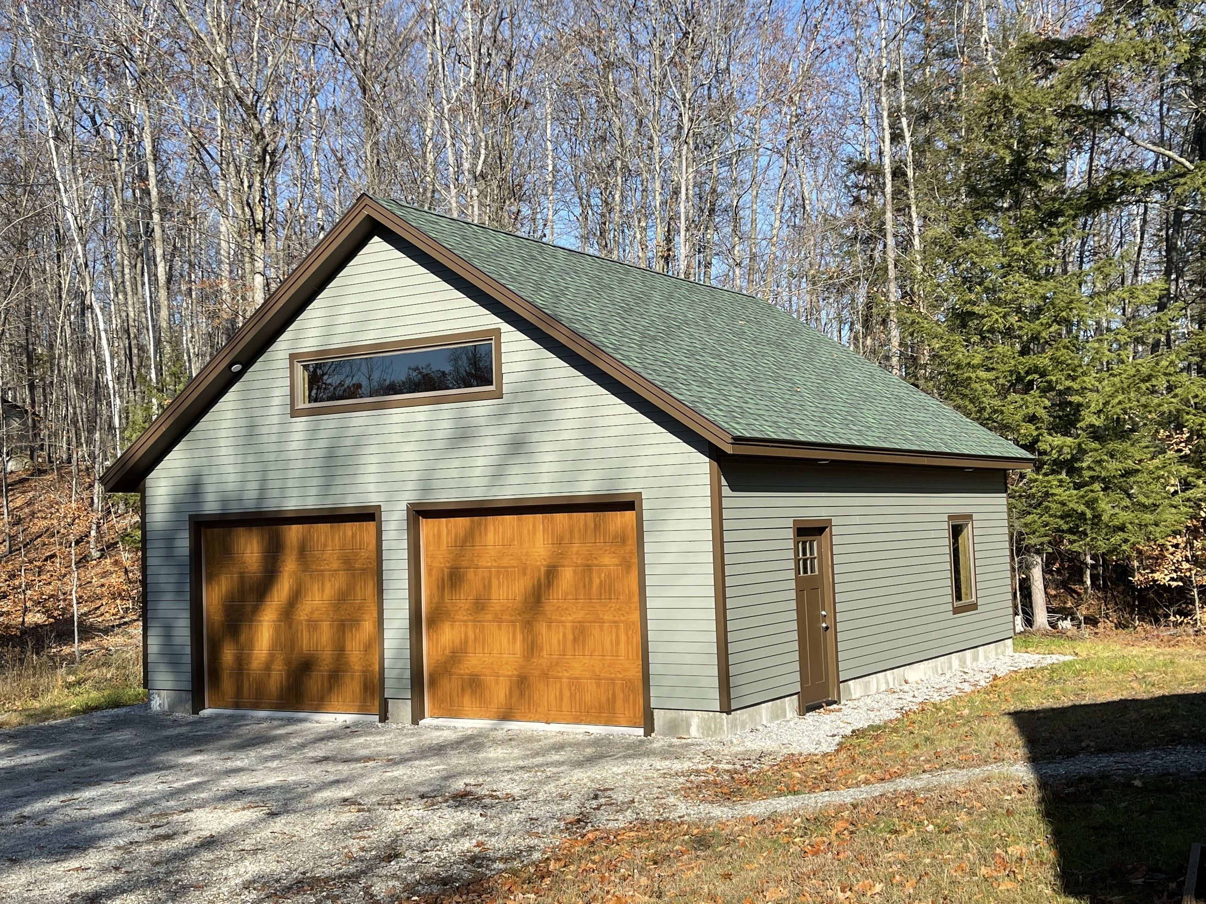 Un garage pour deux voitures, attenant à un bâtiment d’un seul étage, doté d’un toit à pignon et d’une petite fenêtre au-dessus des portes du garage.