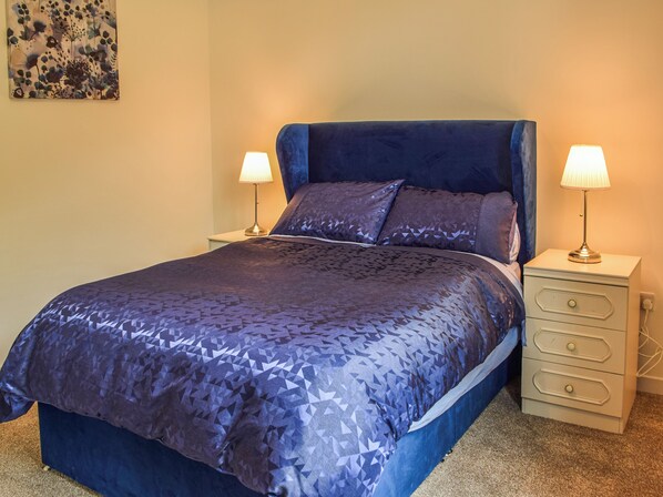 A neatly made bed with a blue headboard and matching pillows, flanked by two bedside tables with lamps.