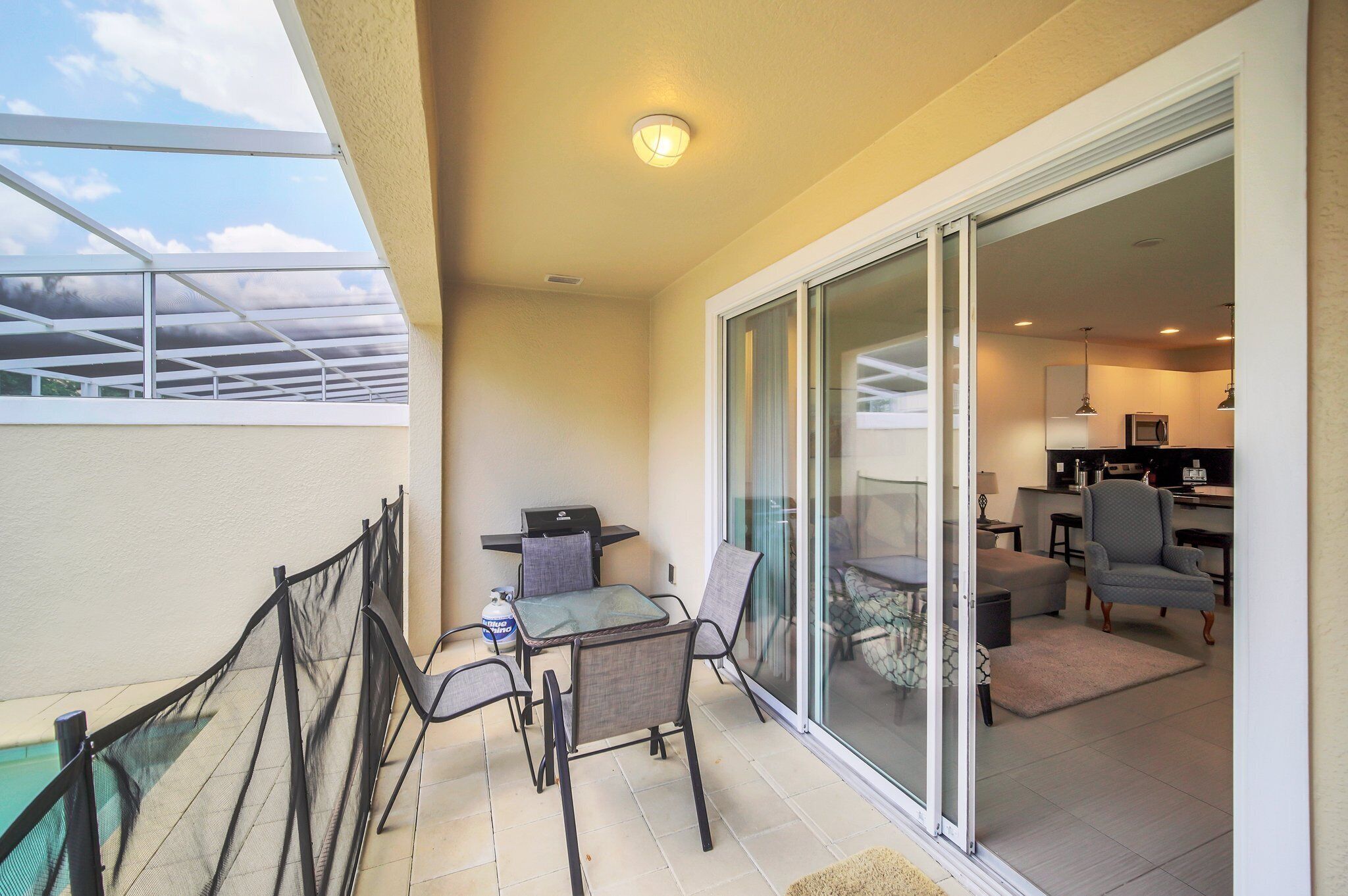 A balcony with a table and chairs, a grill, and a sliding glass door leading to a living area with a kitchen.